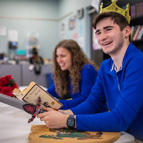 High school boy reading Macbeth and wearing a king's crown